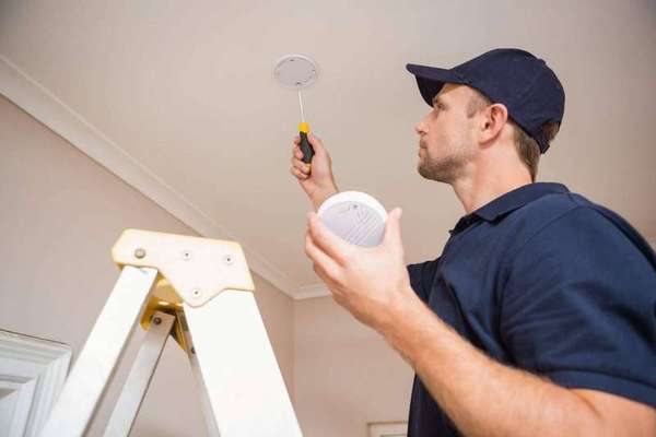 Electrician installing a smoke detector on a home ceiling
